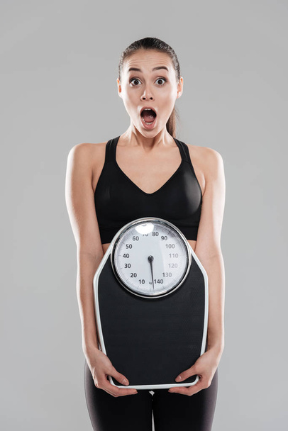 Shocked astonished young woman athlete holding weighing scale - Fotografie, Obrázek