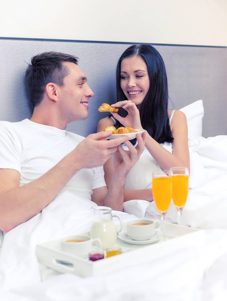 smiling couple having breakfast in bed in hotel - Foto, afbeelding