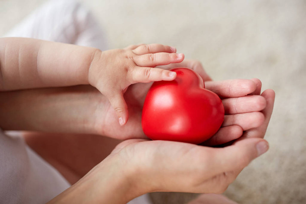 close up of baby and mother hands with red heart - Foto, afbeelding