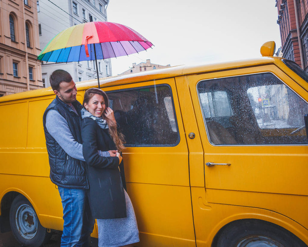 young man and woman with long hair hugging under a bright colored umbrella  smiling against the background of yellow van - Photo, image