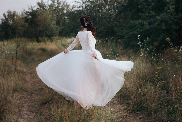 Yong bride spinning in a white dress on the bank on nature - Photo, image