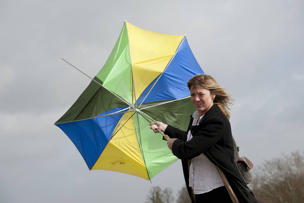 Frau hält an einem windigen Tag einen Regenschirm von innen nach außen - Foto, Bild