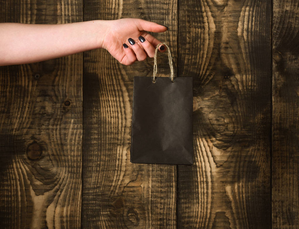 black shopping bag in female hand on wooden background - Фото, зображення