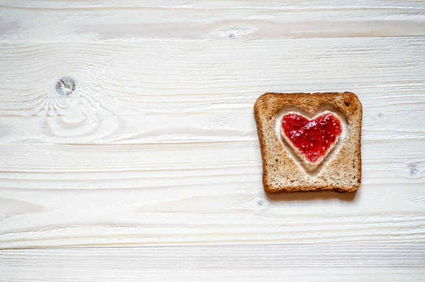 Toasted white bread with a heart inside. At the heart plastered with raspberry jam. - Foto, afbeelding