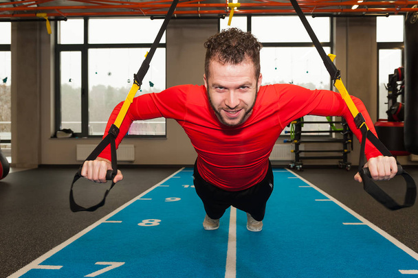 white curly bearded sporty man exercising with trx fitness straps in gym - Zdjęcie, obraz