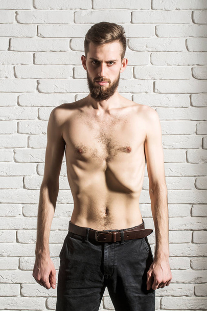 slim bearded man with thin bare torso on brick background - Foto, afbeelding
