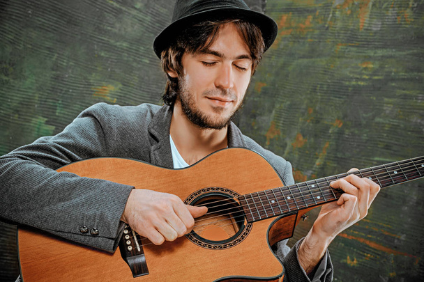 Cool guy with hat playing guitar on gray background - Zdjęcie, obraz