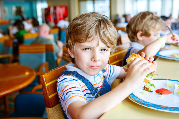 Милый здоровый дошкольник ест гамбургер, сидя в школьной столовой.
 - Фото, изображение