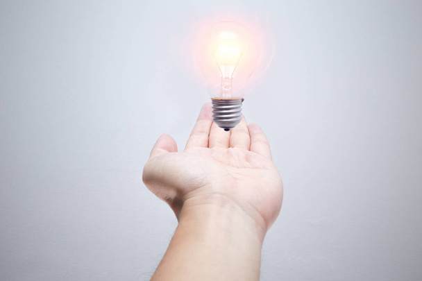 bring idea in your hand. light bulb lighting over male palm on white background - Photo, Image