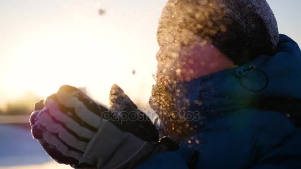 Teenager bläst Schnee mit den Händen auf Sonnenuntergang Hintergrund in Großaufnahme - Filmmaterial, Video