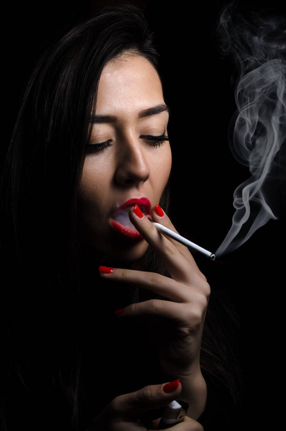 Portrait of the beautiful elegant girl smoking cigarette on black background. - Foto, imagen