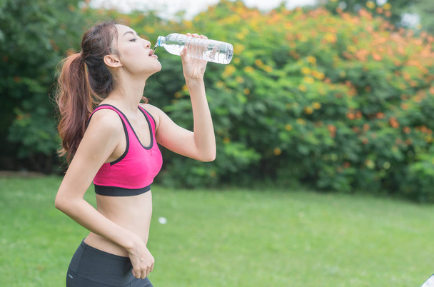 молода приваблива жінка п'є воду з пластикової пляшки в парку
 - Фото, зображення