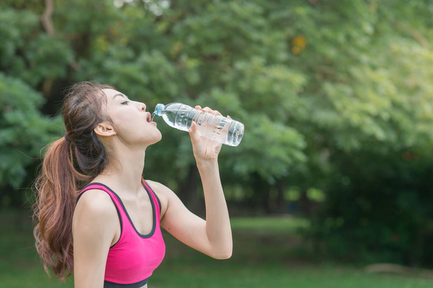 若い魅力的な女性は、公園でペットボトルから水を飲む - 写真・画像