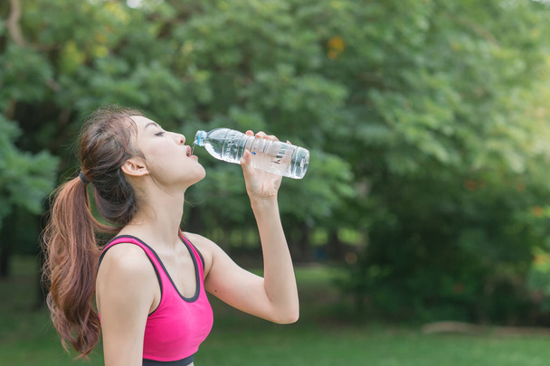 fiatal, vonzó nő ivóvíz műanyag palackból a parkban - Fotó, kép