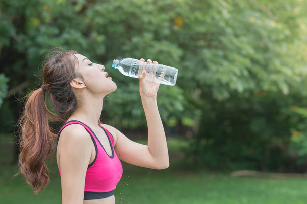 genç çekici kadın içme suyu parkta plastik şişe - Fotoğraf, Görsel