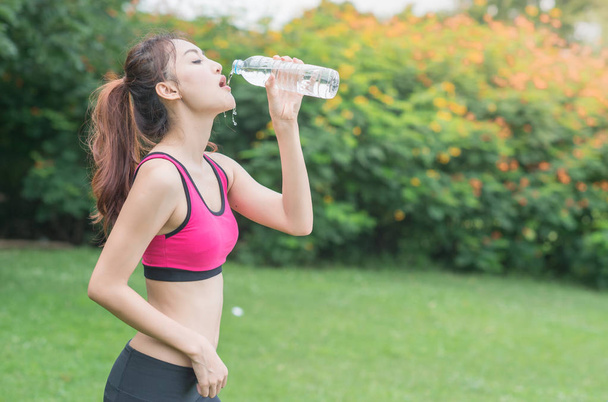 jovem mulher atraente água potável de garrafa de plástico no parque
 - Foto, Imagem