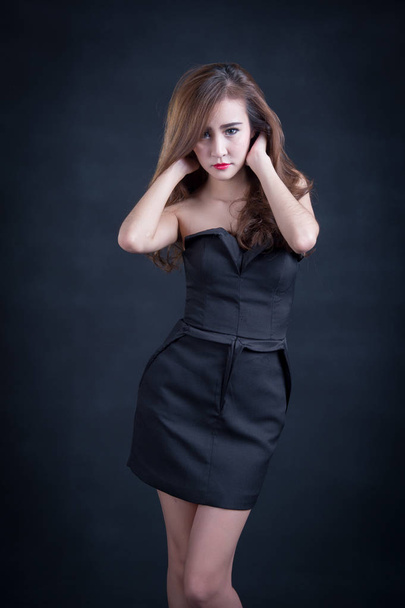 Beautiful sexy woman with perfect slim body and long curly hair in black dress posing over black background. Studio shot. - Photo, image