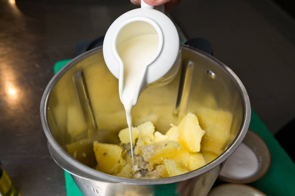 Close up shot of a jug of cream, being poured onto fluffy peeled potatoes in a blender. - Photo, image
