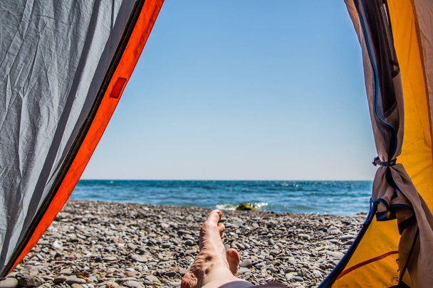 Image jambes humaines couchées dans une tente touristique avec vue sur la mer
 - Photo, image