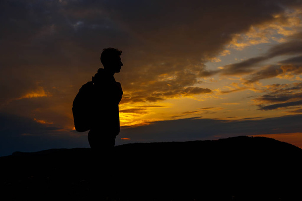 Sylwetki turysty z plecakiem cieszącym się widokiem na zachód słońca ze szczytu góry - Zdjęcie, obraz