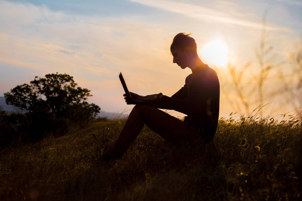 silhouet van gelukkige zakenman met laptop aan het werk op het veld - Foto, afbeelding
