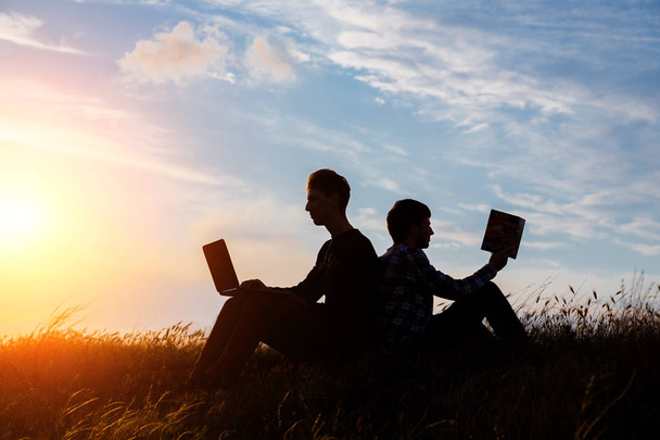 силуэт мужчины с ноутбуком и книгой на фоне заката или восхода солнца - Фото, изображение