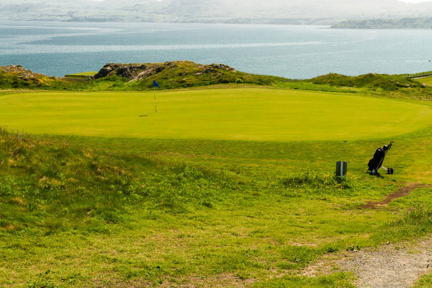 Поле для гольфа, зеленое море на заднем плане и сумка для гольфа
. - Фото, изображение