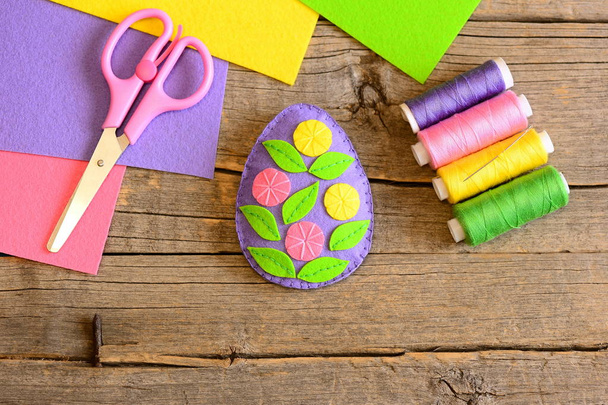 Huopa pääsiäismuna koristeltu kukkia ja lehtiä. Yksinkertainen pääsiäisalus toimintaa. Opetan lapsille ompelutaitoja. Sakset, lanka pakki, värillinen huopa levyt puinen tausta kopioi tilaa
  - Valokuva, kuva