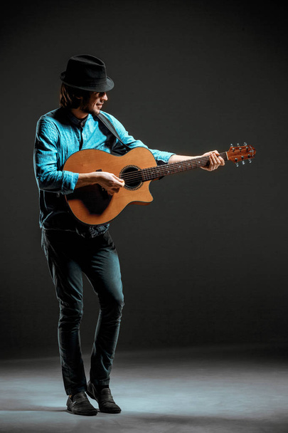 Cool guy standing with guitar on dark background - Foto, afbeelding