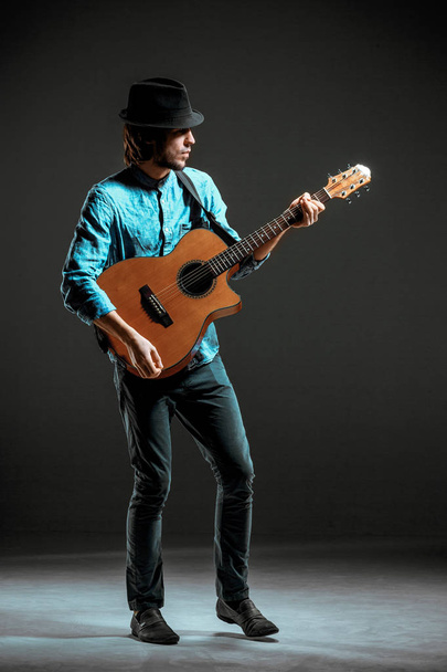 Cool guy standing with guitar on dark background - Photo, Image