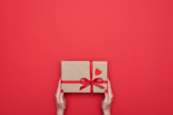 Female hands holding gift package wrapped with red ribbon - Φωτογραφία, εικόνα