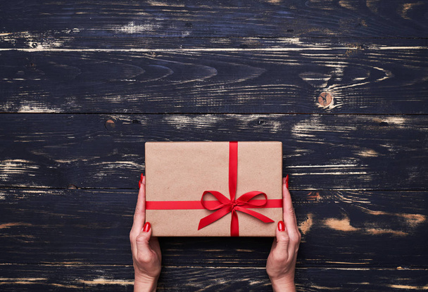 Duas mãos segurar uma caixa de presente agradável amarrado com fita vermelha
  - Foto, Imagem