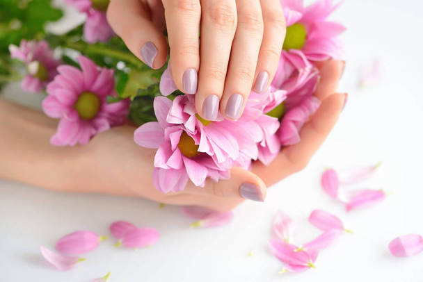 Hände einer Frau mit rosa Maniküre auf Nägeln und rosa Blumen auf weißem Hintergrund - Foto, Bild