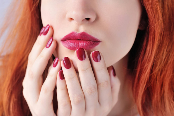 Beautiful red-haired young woman with dark red manicure, lipstick same color. Close up Portrait. - Фото, изображение