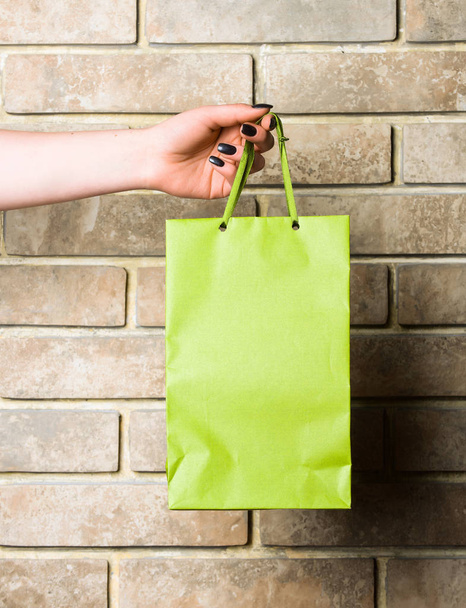 green shopping bag in female hand on brick wall - Foto, imagen