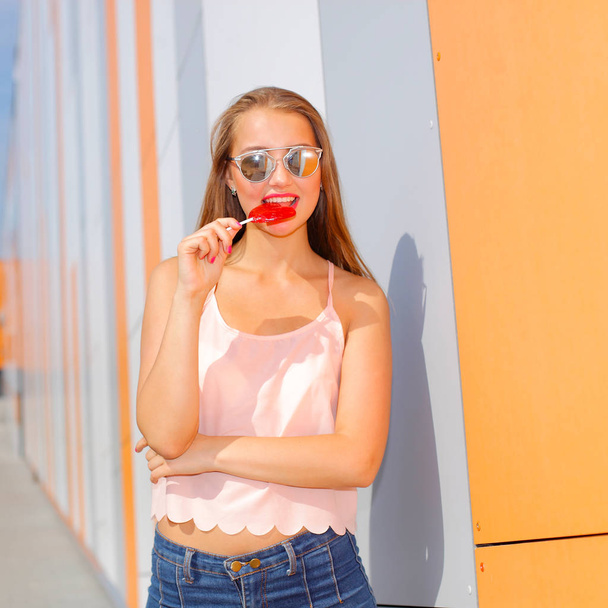 Cheerful girl in sunglasses have fun with candy in her hands - Фото, изображение