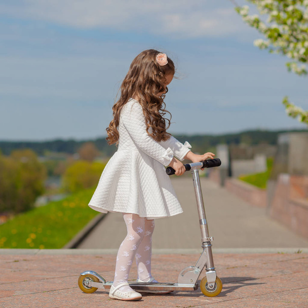Menina jogando ao ar livre e montando uma scooter
 - Foto, Imagem