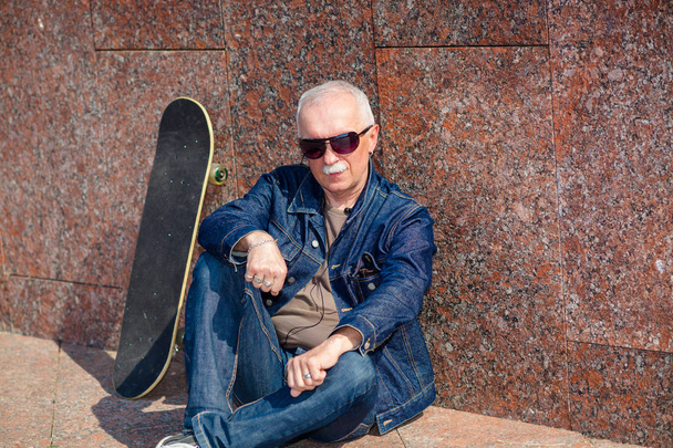 Vanhempi mies istuu ja haaveilee kadulla lähellä rullalauta
 - Valokuva, kuva