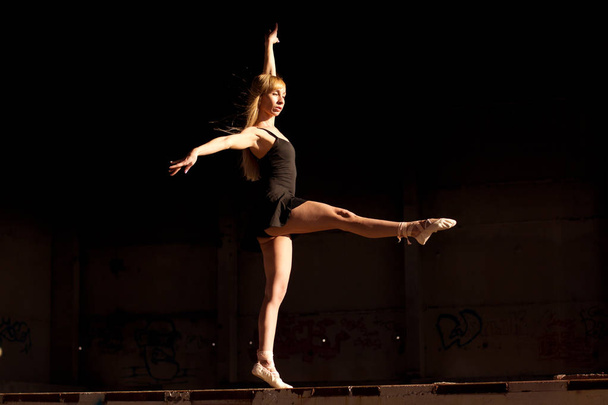 Absolutely stunning perfomance. Ballerina dances in the dark abandoned plant building in a sunlight. - Fotó, kép