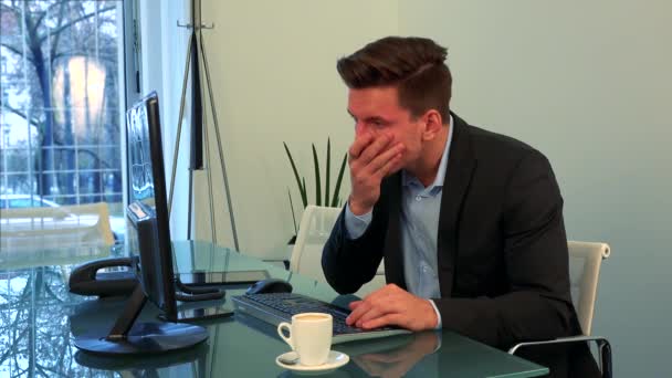 若く、ハンサムな男がオフィスのコンピューターの前に座っているし、彼の手のひらで顔を覆う - 映像、動画