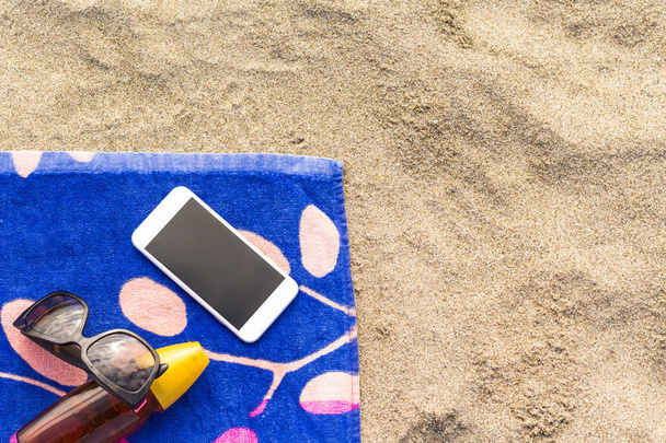 Cep telefonu ile bir plaj havlusu üzerinde güneş koruyucu bir şişe - Fotoğraf, Görsel