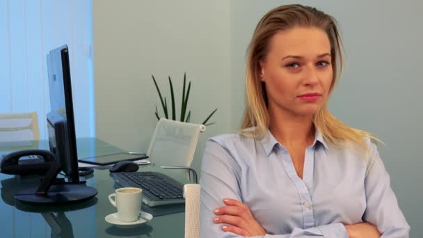Een jonge, mooie vrouw zit op een bureau in een kantoor, kijkt naar de camera en schudt haar hoofd - Video