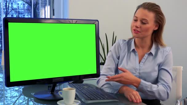 Una joven y hermosa mujer se sienta en un escritorio en una oficina y habla con la cámara, una pantalla de ordenador verde a su lado se volvió hacia la cámara
 - Imágenes, Vídeo