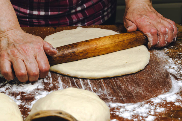 Rolling pin in hands, rolling dough on the wooden table, close-up. - Foto, afbeelding