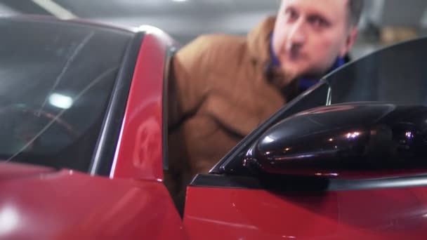 Człowiek z dostaniem czerwony sport samochód po stronie kierowcy. Widok zbliżenie - Materiał filmowy, wideo