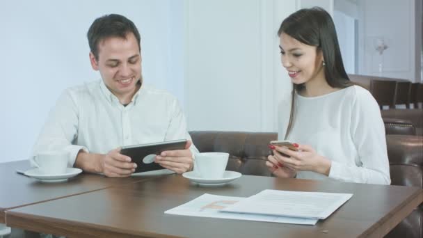 Mosolygó fiatal ember bemutató valamit a Tablet tartja a telefont ebédidőben női munkatárs - Felvétel, videó