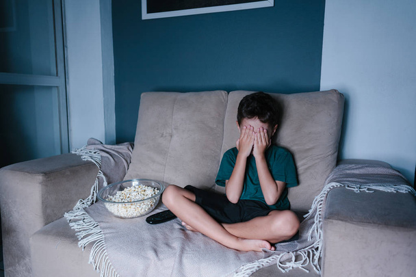 Scared child watching scary movie on tv, sitting on the couch at night - Fotó, kép
