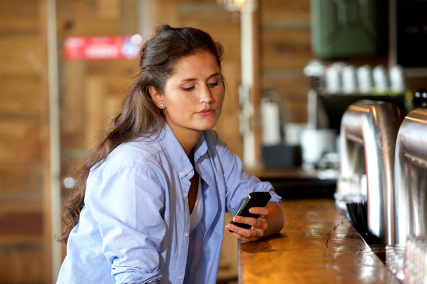молодая женщина в баре с помощью мобильного телефона
 - Фото, изображение