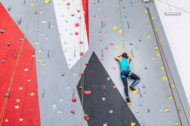Young woman climbing up on practice wall at indoors gym, rear view - Photo, Image