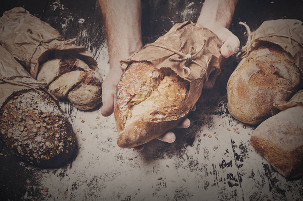 Bakery concept background. Hands hold bread loaf - Фото, изображение